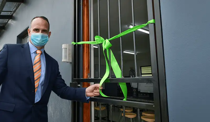 Image of a man in a suit holding the end of a green ribbon that is on the security gate of a classroom | New school Computer Centre to have a ripple effect | CA&S Group
